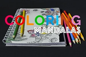 Renkli kalemlerle çevrili, kısmen boyanmış mandala desenli bir defter