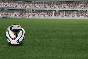 Yeşil çim saha üzerinde bir futbol topu ve arka planda bulanık görünen dolu tribünler