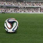 Yeşil çim saha üzerinde bir futbol topu ve arka planda bulanık görünen dolu tribünler