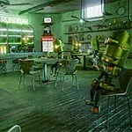 Yeşil tonlarında aydınlatılmış bir kafede robotlar oturuyor, masaların üzerinde yiyecek ve içecekler bulunuyor