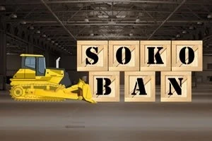 Kapalı bir depoda, üst üste konulmuş SOKOBAN yazılı ahşap kutuların yanında duran sarı bir buldozer